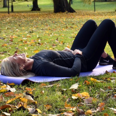 Träningsklädd kvinna ligger på yogamatta på gräsmatta med höstlöv, tema utmattningssyndrom. stress.