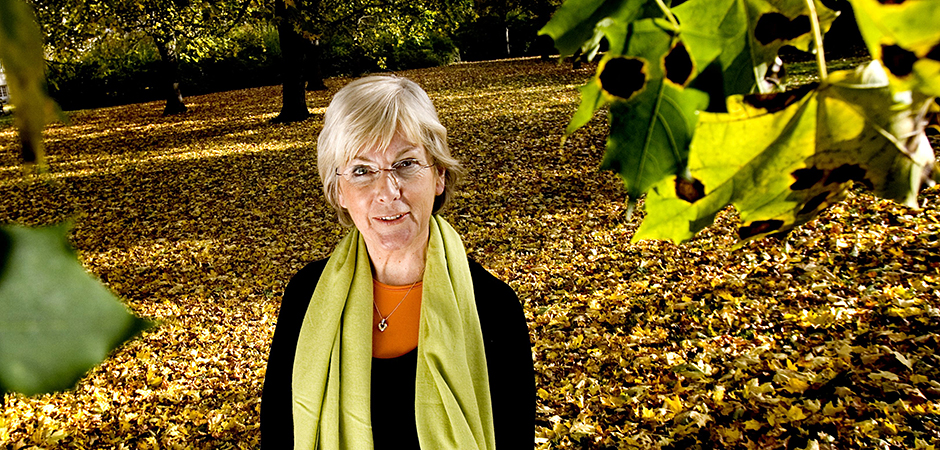 Eva Vingård står in park med gröna blad i förgrunden och höstlöv på marken