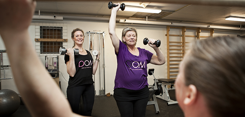 Två kvinnor står bredvid varandra och tränar med handlar i en gymmiljö.