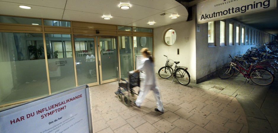 En sjuksköterska kör en rullstol in en sjukhusentré.