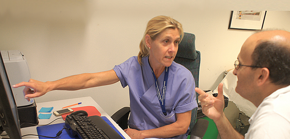 Kvinna i sjukhuskläder pekar på en datorskärm och samtalar med en patient.
