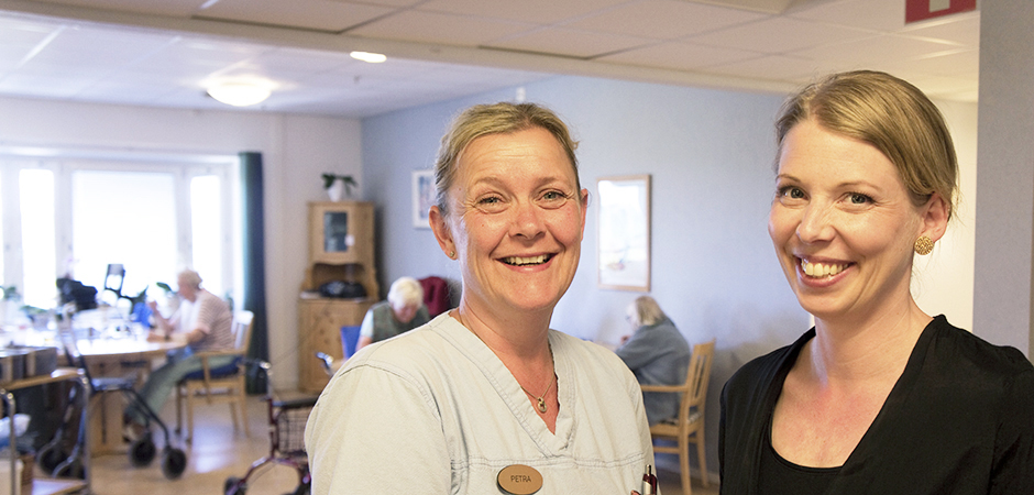 Två kvinnor står bredvid varandra och ler i en vårdmiljö.