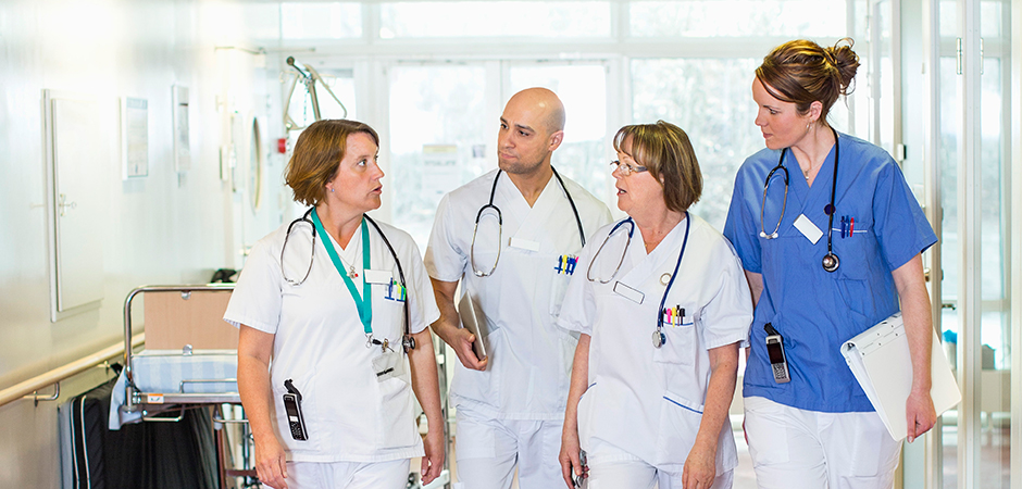 Fyra personer i sjukhuskläder och stetoskop står bredvid varandra i en sjukhuskorridor.