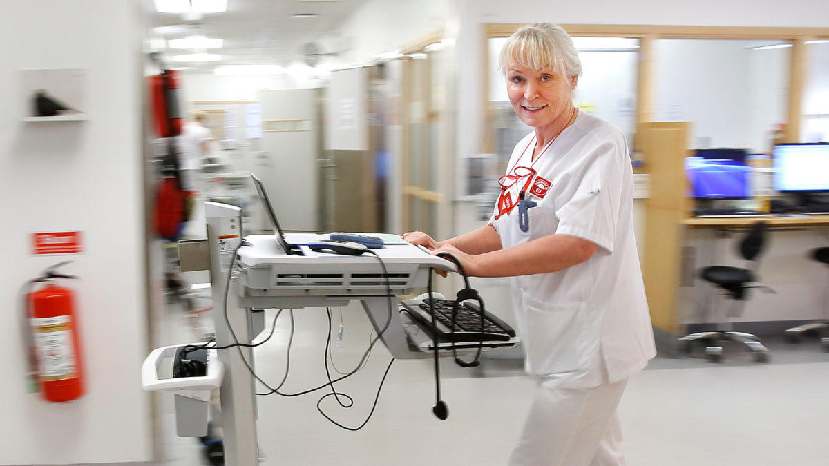 Läkaren Kerstin Skog Tigerström i sjukhuskläder står vid ett arbetsbord i en sjukhuskorridor.