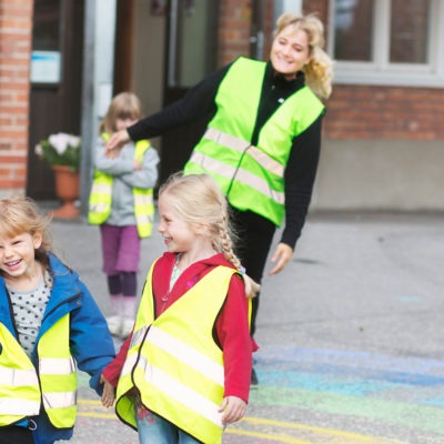 Pedagog och tre barn i gula reflexvästar leker på gård.