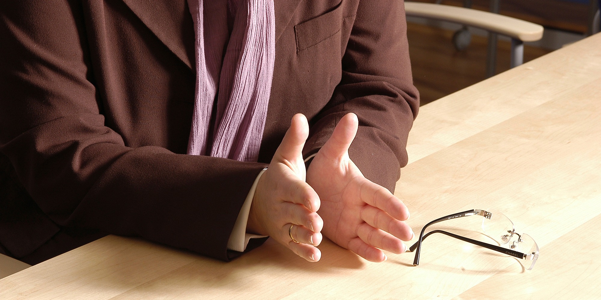 Närbild av en persons händer på ett bord. Glasögon ligger bredvid