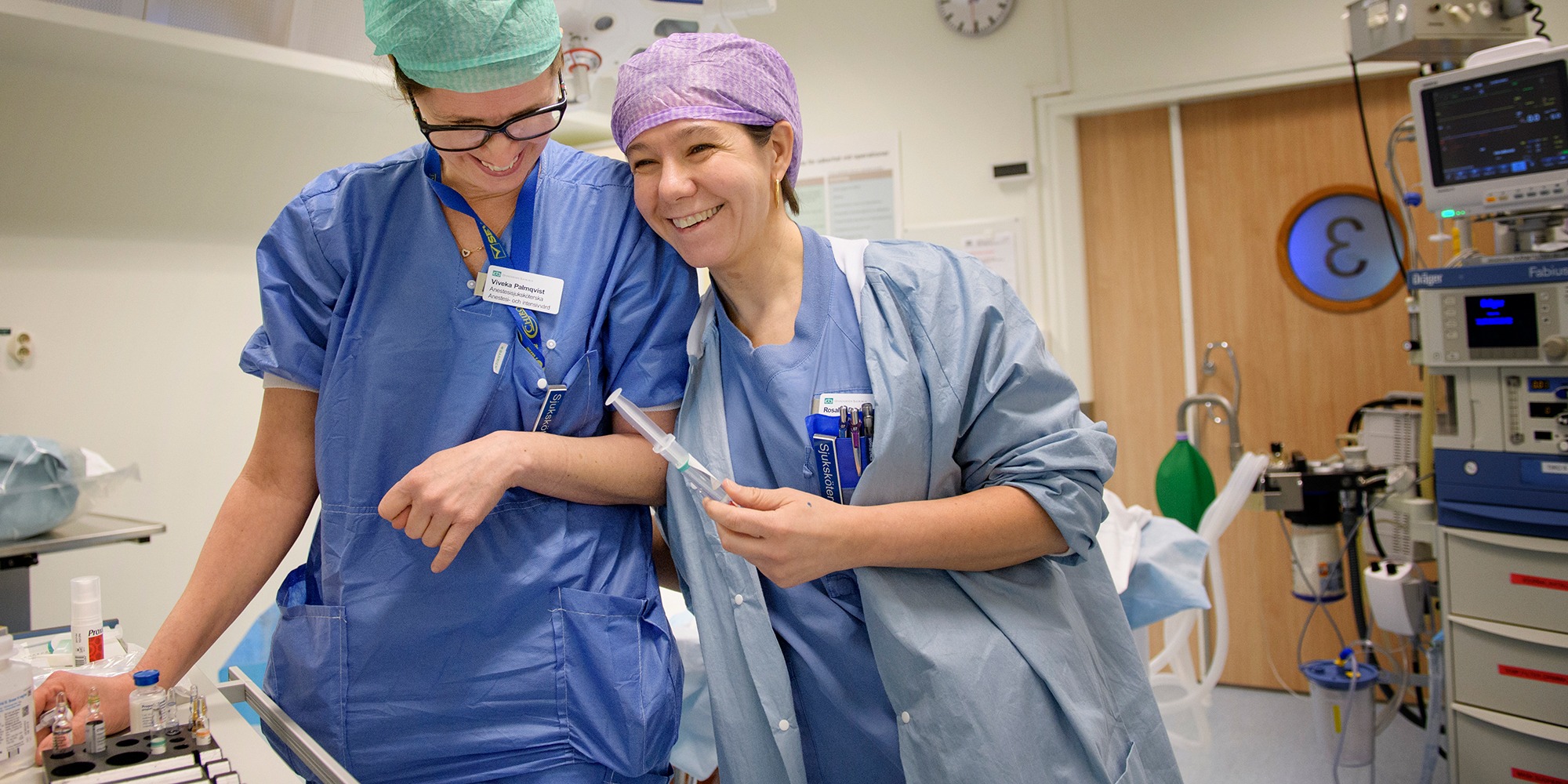 Två kvinnor i sjukhuskläder skrattar tillsammans i operationssal.