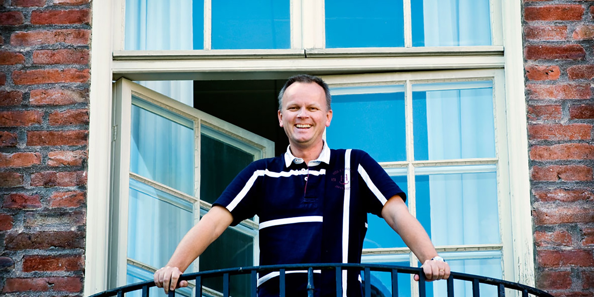 Porträtt av Jan Gulliksen ståendes på en balkong med fönsterdörr i bakgrunden.