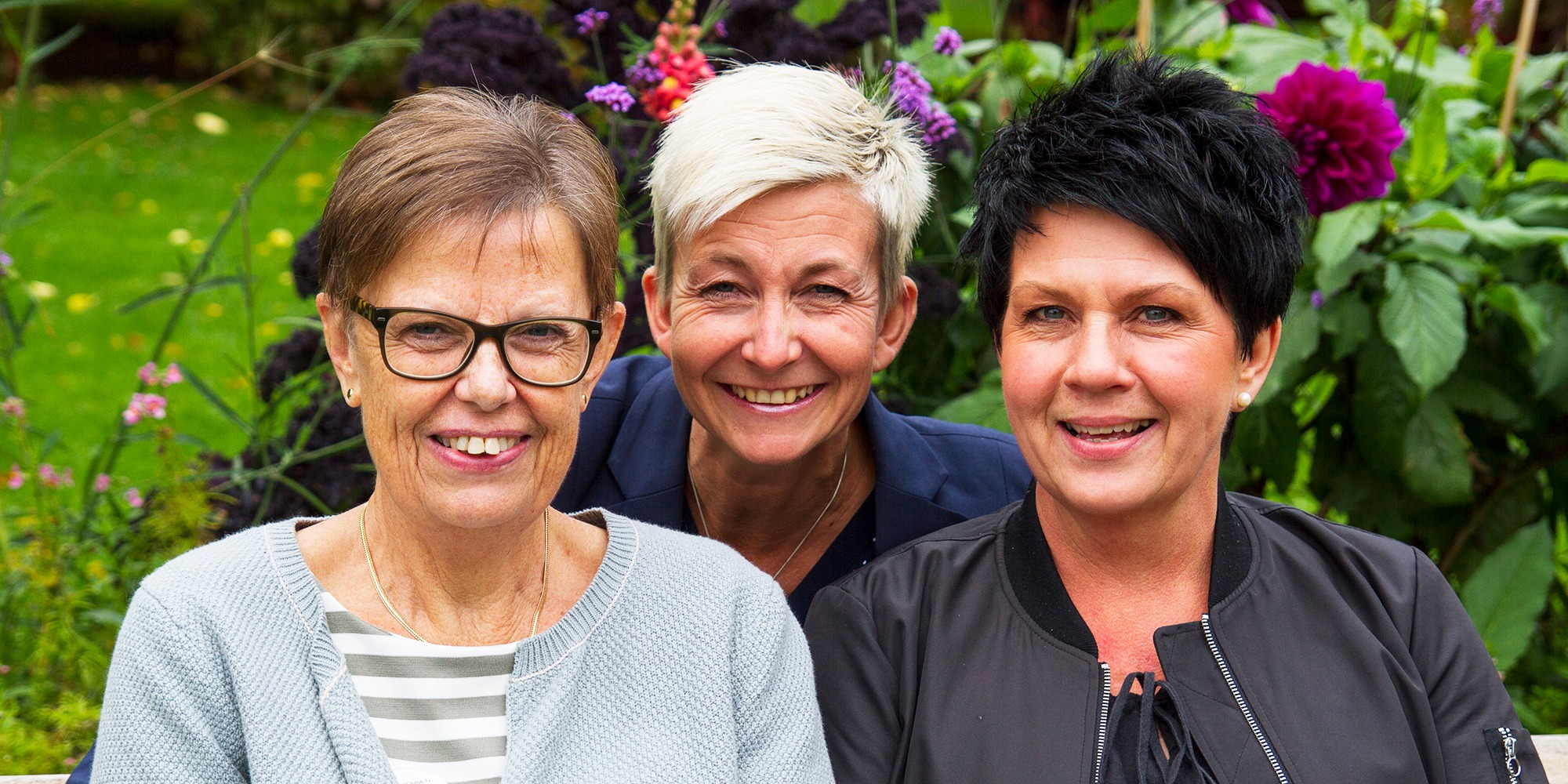 Närbild på tre leende kvinnor, Elisabet Björklund, Marie Niljung och Ingela Persson, i park med blommor i bakgrunden