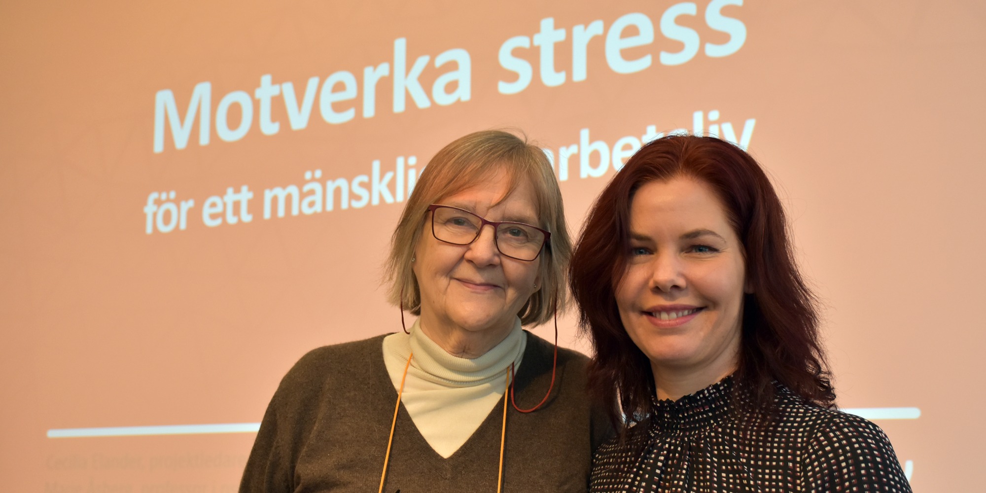 Marie Åsberg och Cecilia Elander ler in i kamera framför stor skärm där det står motverka stress