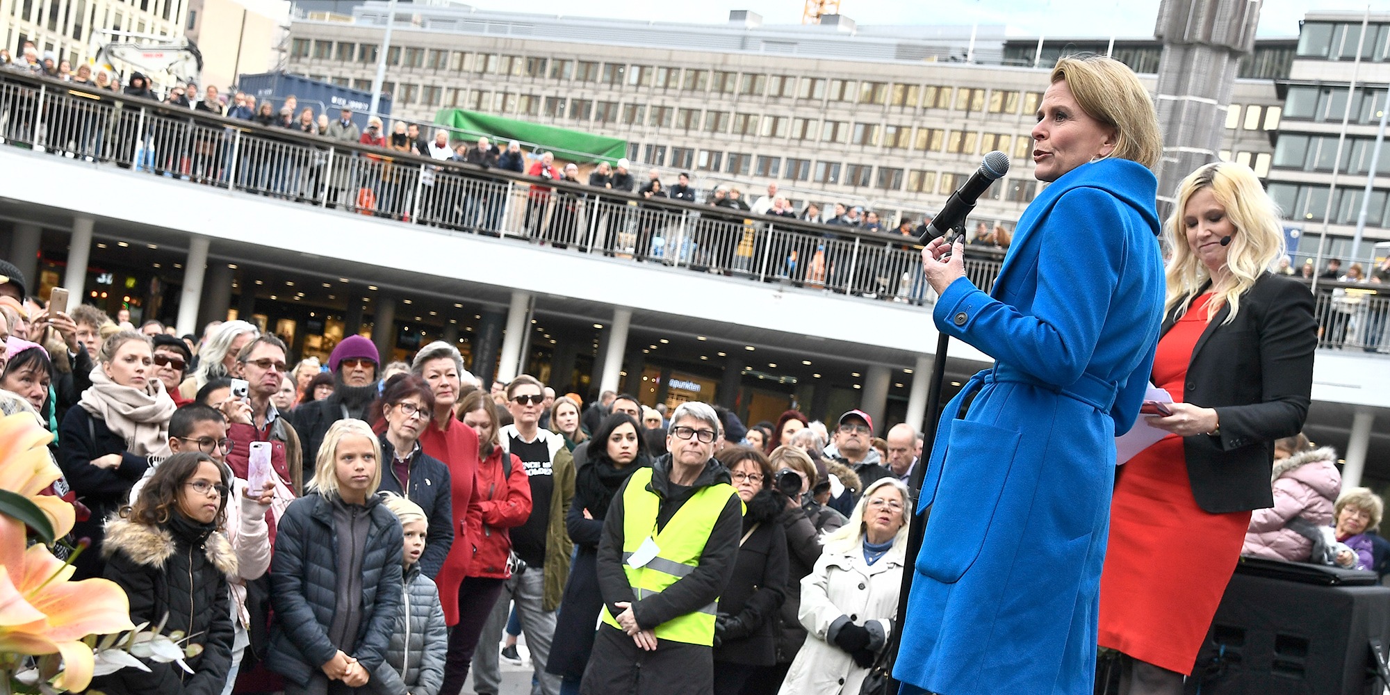 manifestation på¨sergels torg med jämställdhetsminsiter Åsa Regner i blå kappa i förgrunden, fotad snett nedifrån. publik med många barn och kvinnor framför scenen.