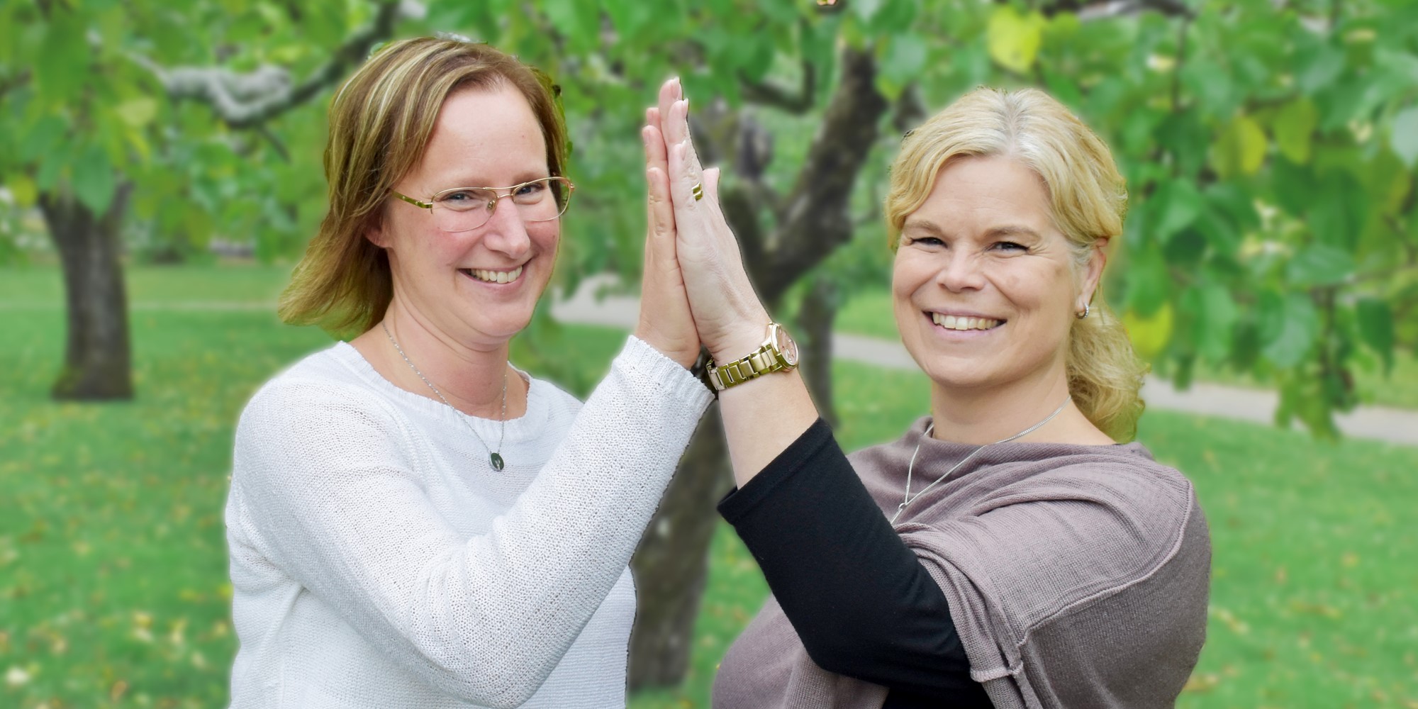 susanne persson och sofia johansson står på en gräsmatta och gör high five mot varandra. de är glada. susanne persson har en vit tröja, sofia johansson har en grå tröja.