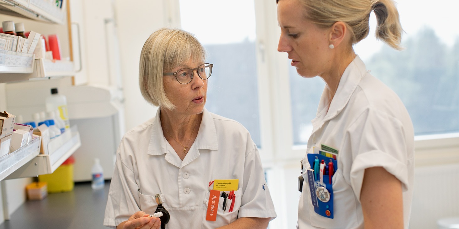 Apotekare Gerd Petersson visar sjuksköterska Ulrika Alegrievski något framför en läkemedelshylla