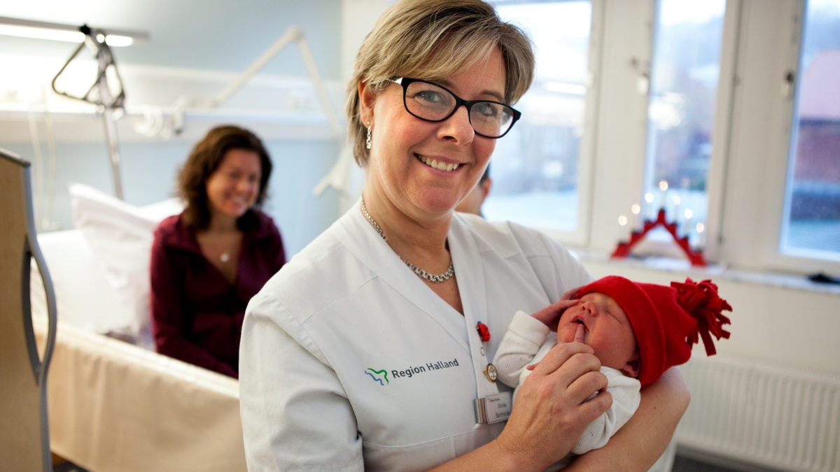 Barnmorska Annika Neij håller nyfödd bebis med röd mössa, tema jul på jobbet