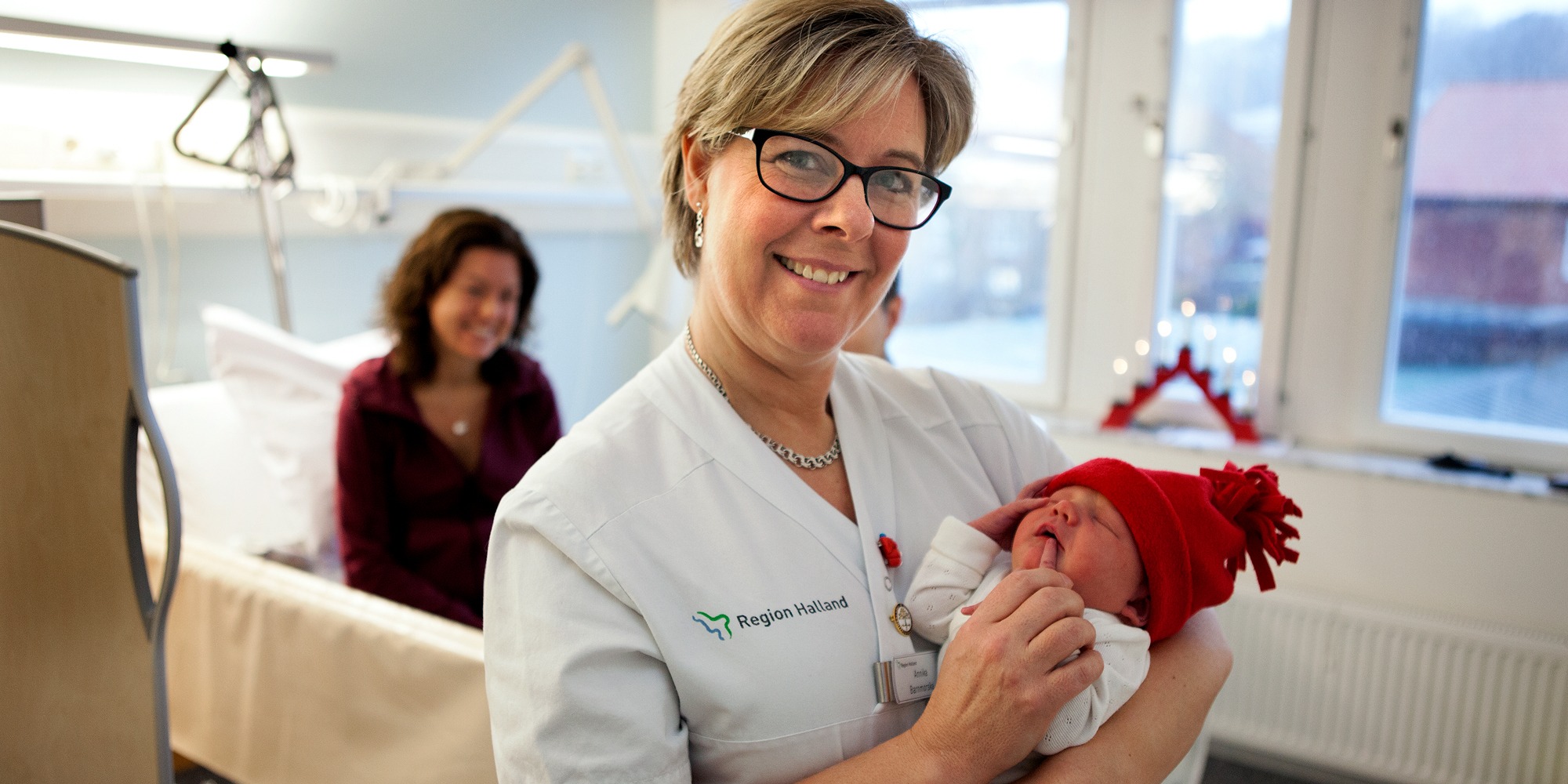 Barnmorska Annika Neij håller nyfödd bebis med röd mössa, tema jul på jobbet