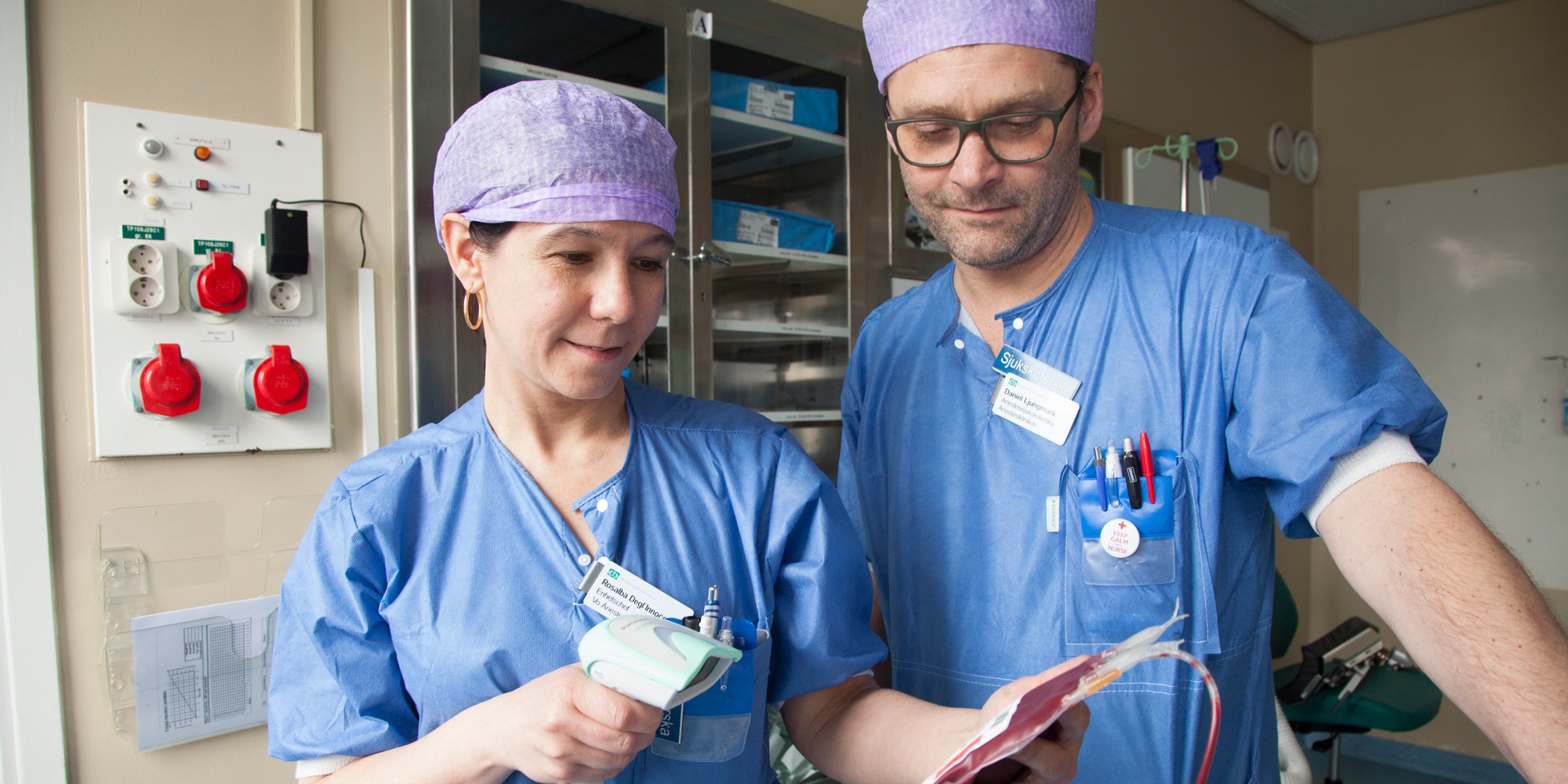 Kvinna sjuksköterska håller i blodpåse och scanningsapparat, kollega man sjuksköterska står bredvid, Arbetsmiljölyftet