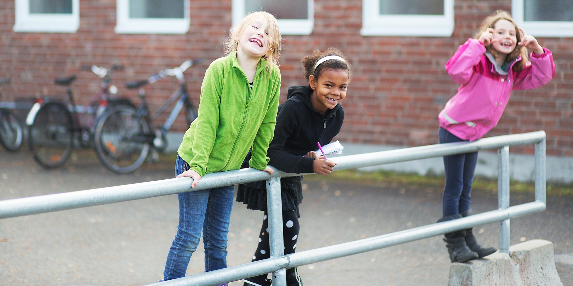 Två glada lågstadiebarn lutar sig mot ett räcke på en skolgård.