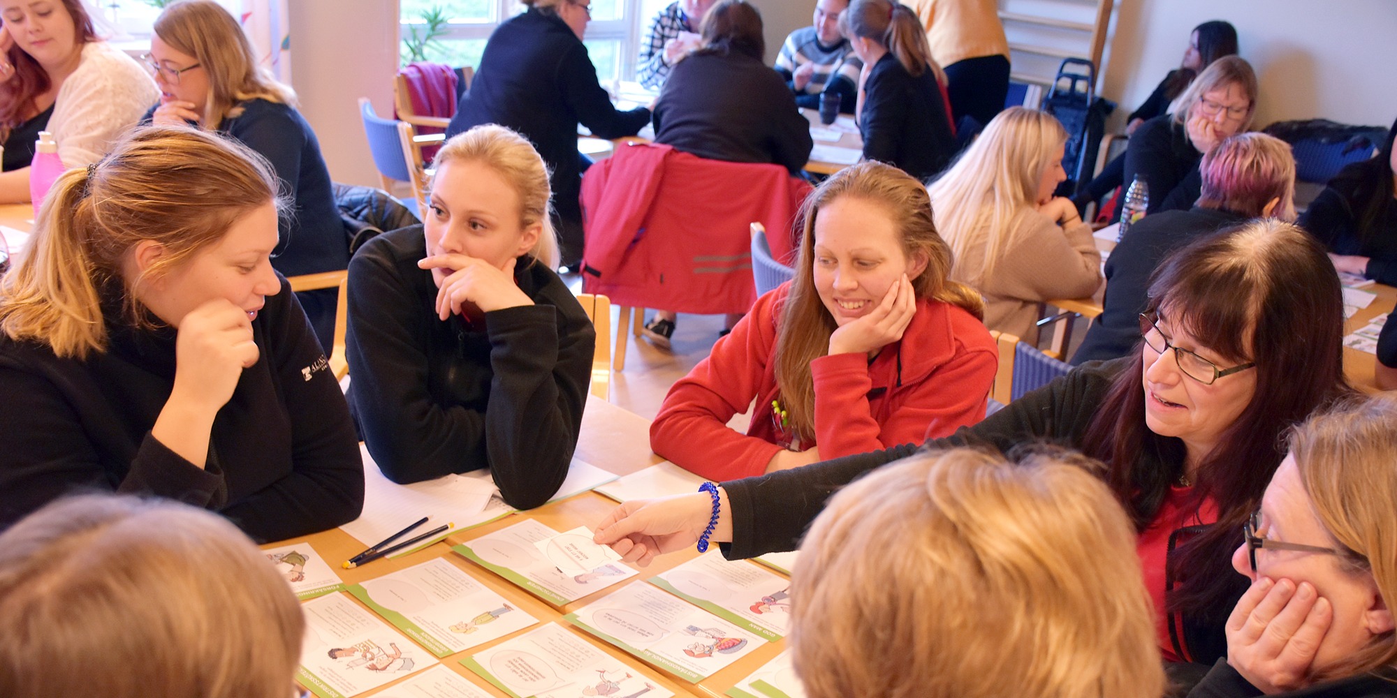 Hemtjänstmedarbetare samtalar gruppvis runt bord med diskussionsmaterial, verktyget Vård i annans hem