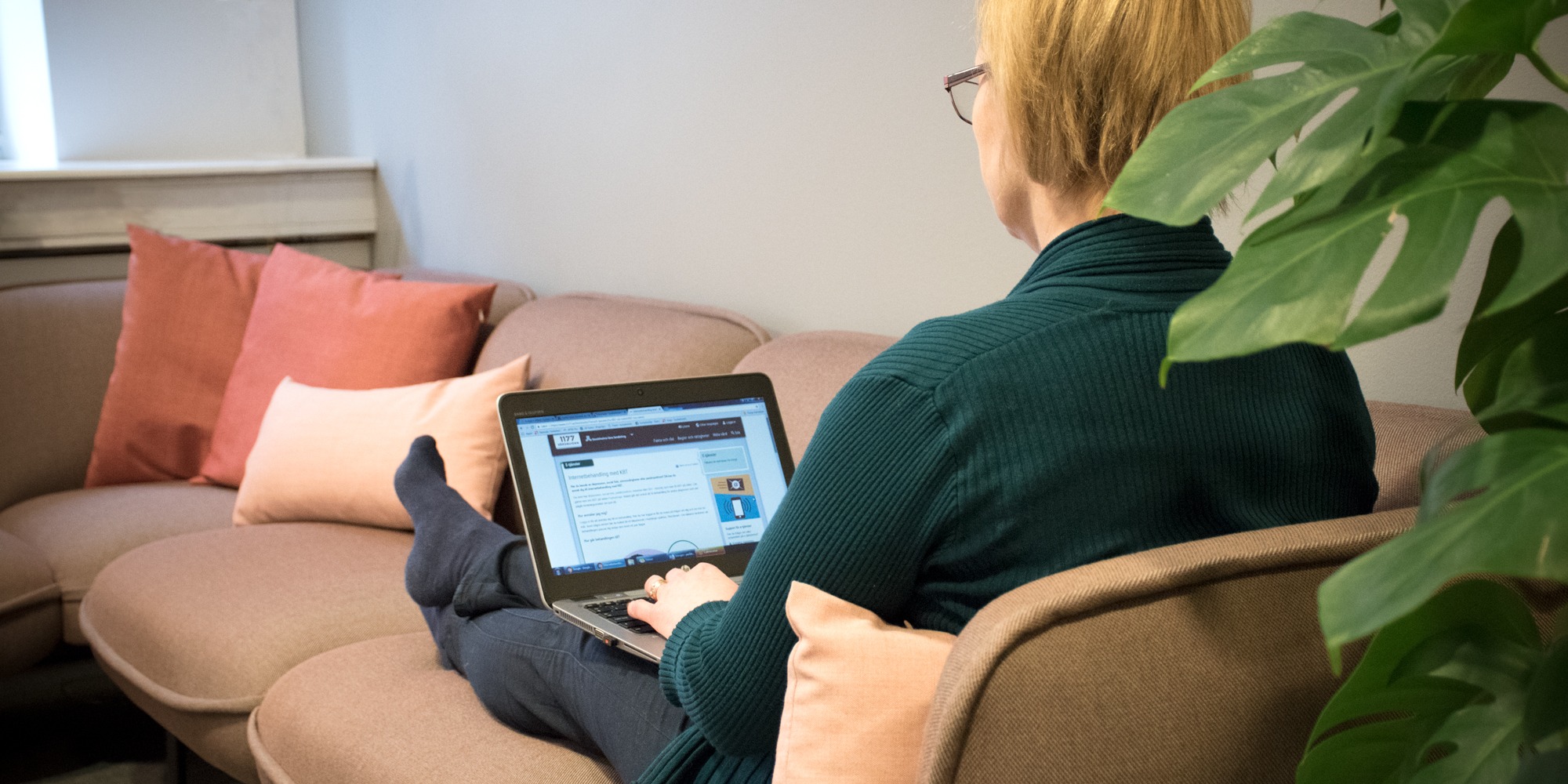 Kvinna sitter i soffa med laptop i knät, webbterapi