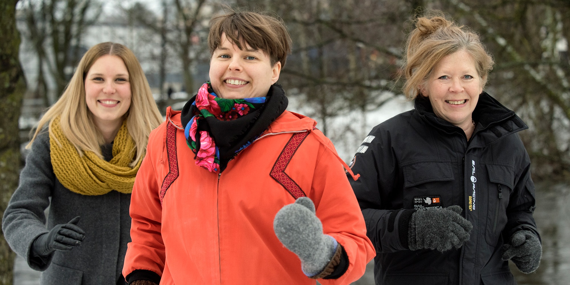 tre glada vinterklädda kvinnor springer utomhus.