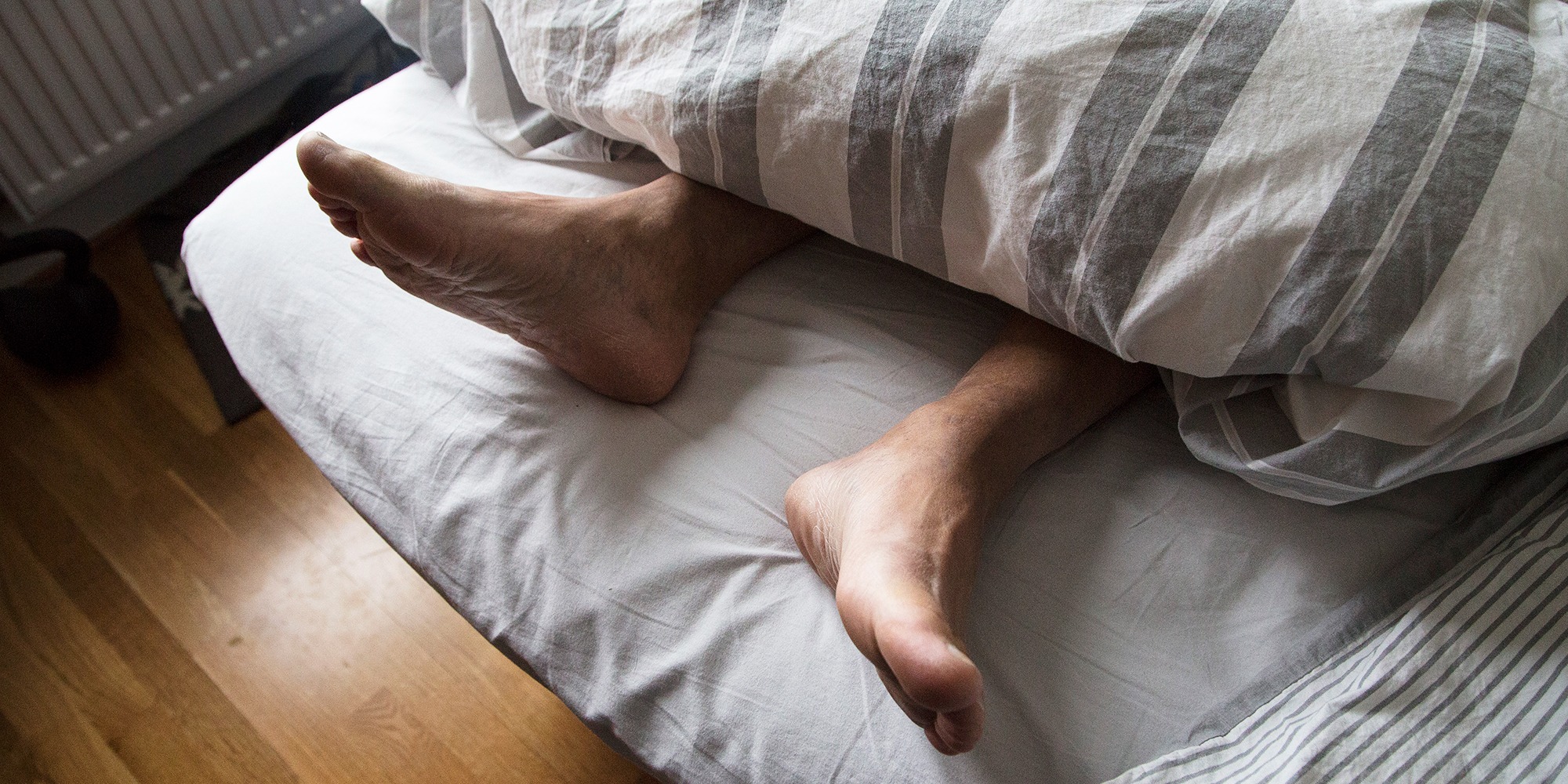 två fötter sticker ut under ett täcke vid fotändan av en säng.
