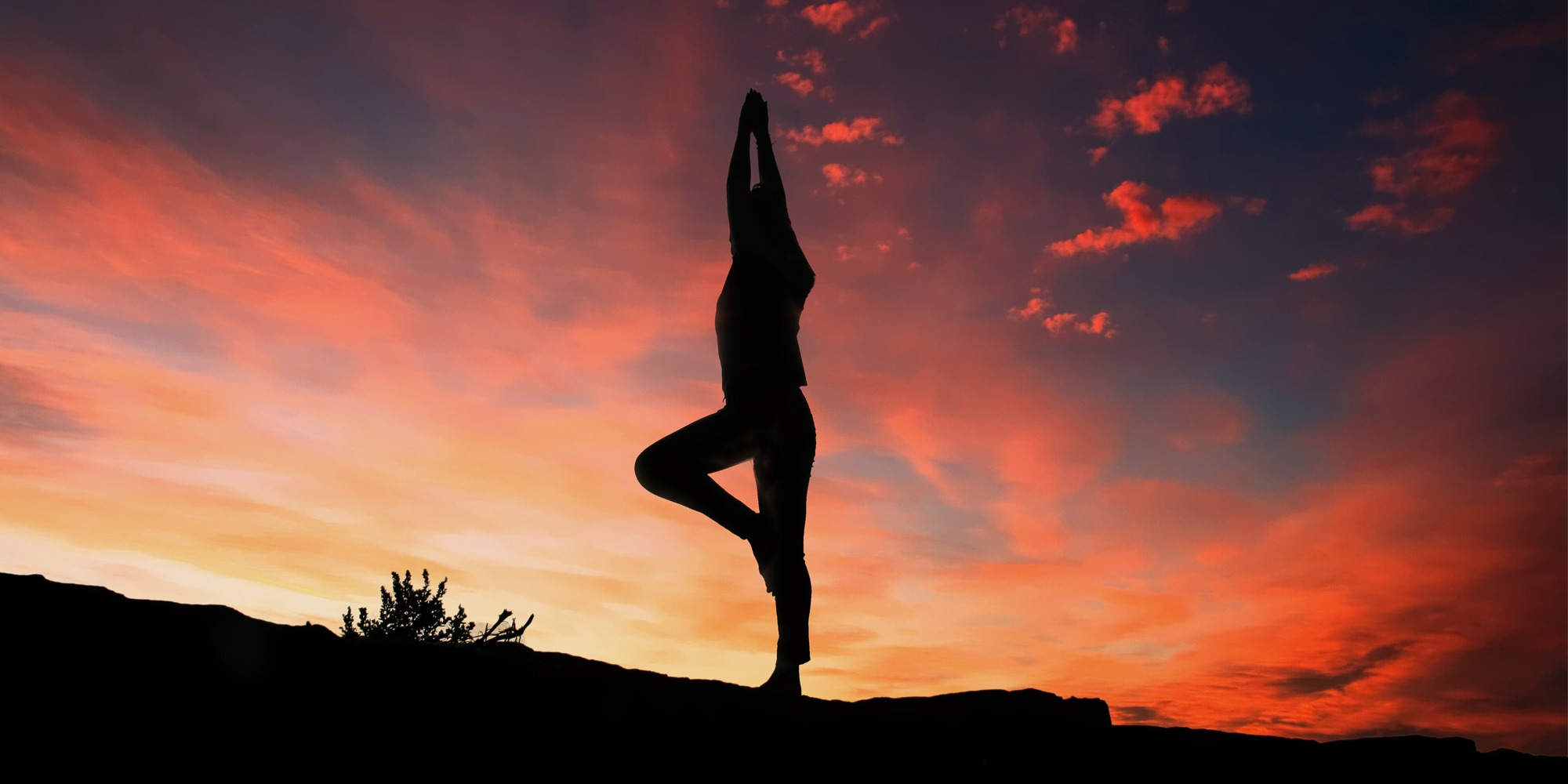 Svart siluett av en person som utövar yoga. Bakgrunden är en brandgul himmel.