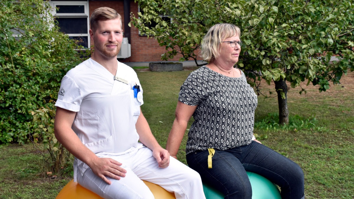 Fysioterapeut och sekreterare sitter på varsin pilatesboll i trädgård utanför vårdcentral, återhämtning i arbetet.