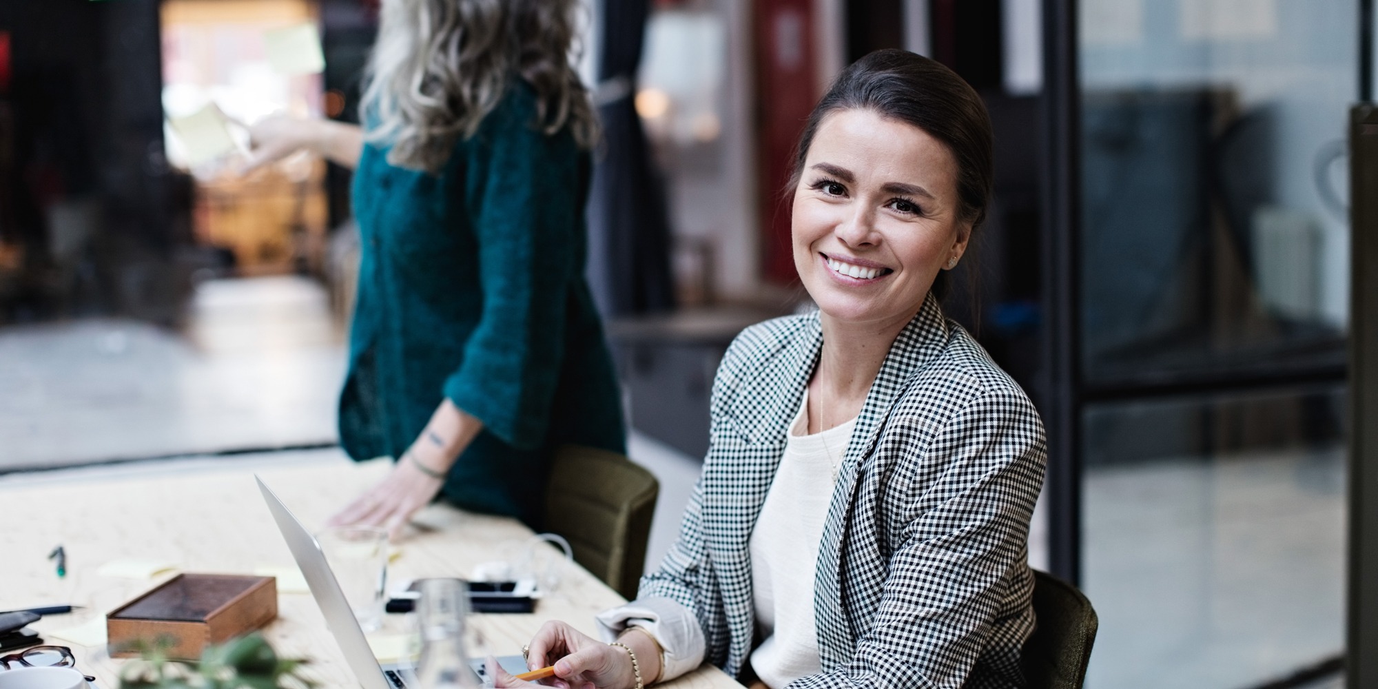 Leende mörkhårig kvinna vid bord under möte med kollegor på kontor, socialsekreterares arbetsmiljö.