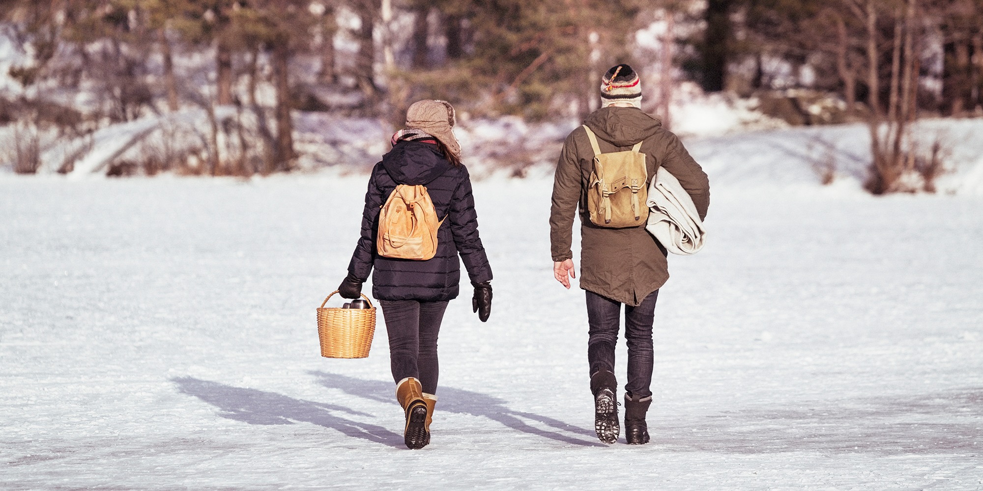 vinter. Två personer går med ryggen mot kameran, på isen, i sol. ryggsäckar och kaffekorg.
