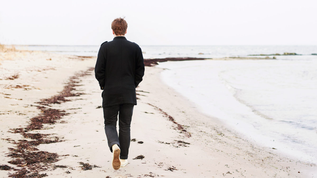 En man i jacka och långbyxor går på en höstlik strand