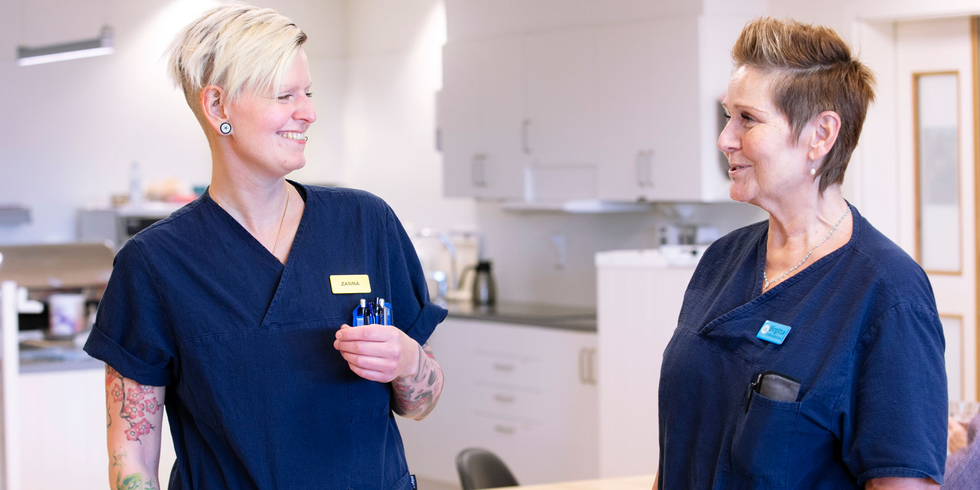 Zanna Zachrisson Ström och Birgitta Ström, klädda i blå arbetskläder, tittar på varandra, på ett särskilt boende för äldre i Sala.