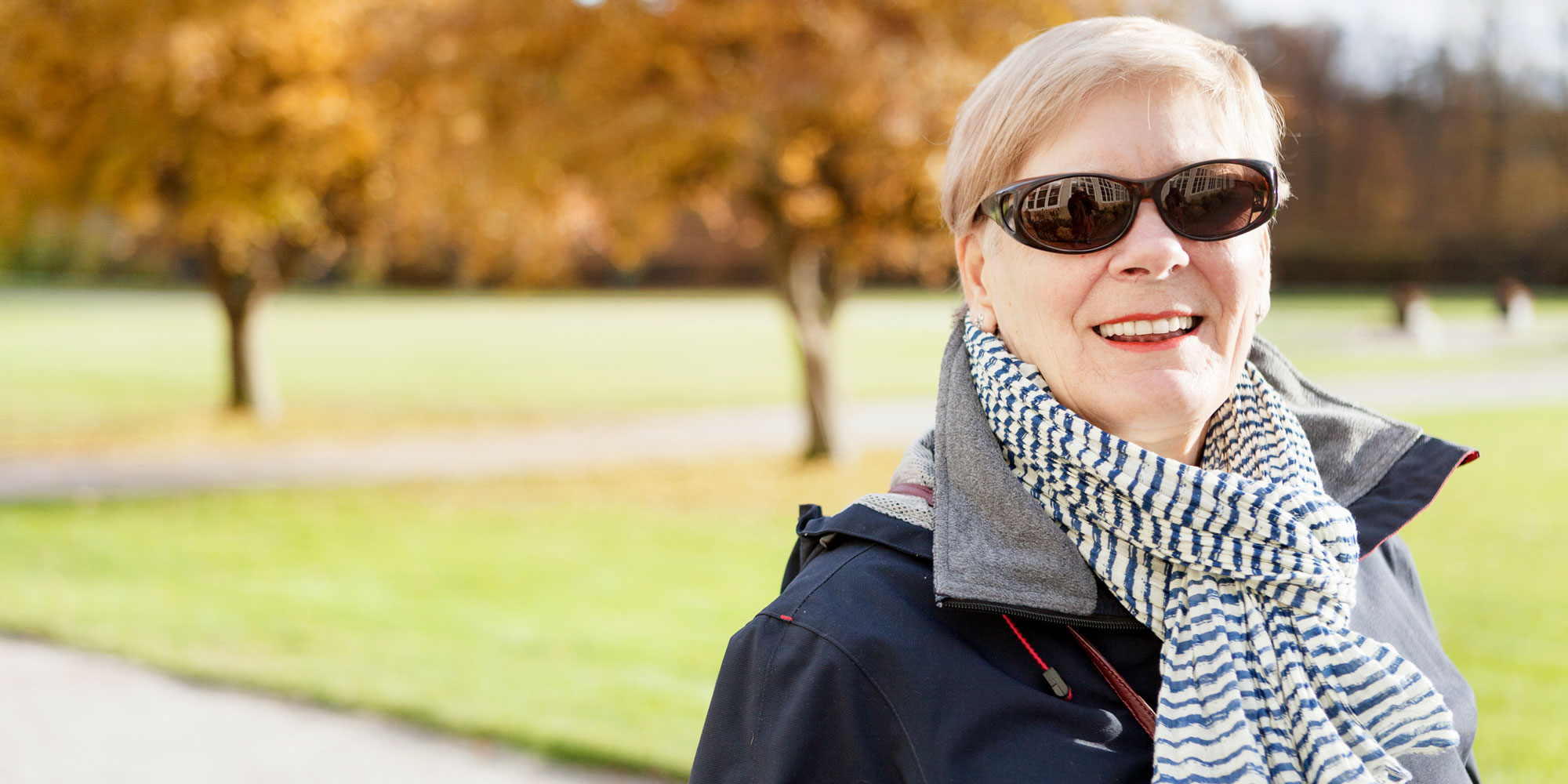 Halvporträtt på kvinna med solglasögon som går ute i en park.