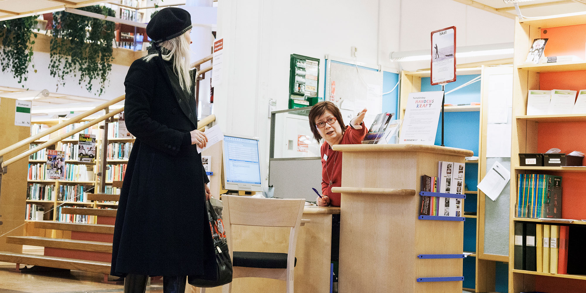 Besökare och personal vid infodisk på bibliotek.