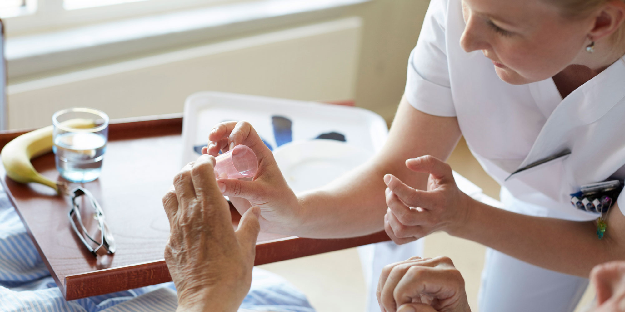 Sjuksköterska ger medicin till patient i säng.