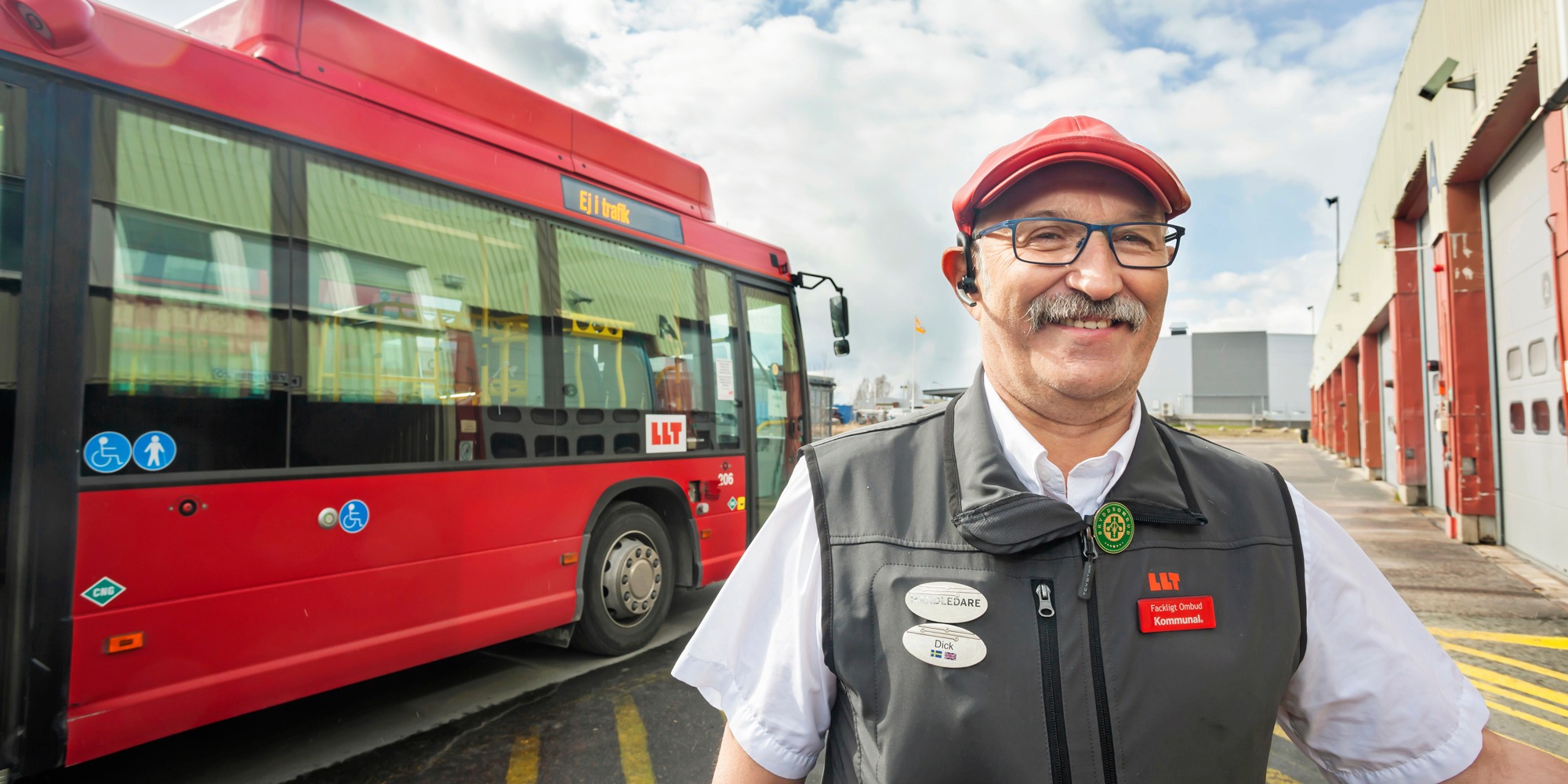 En busschaufför står framför en buss och ler mot kameran.