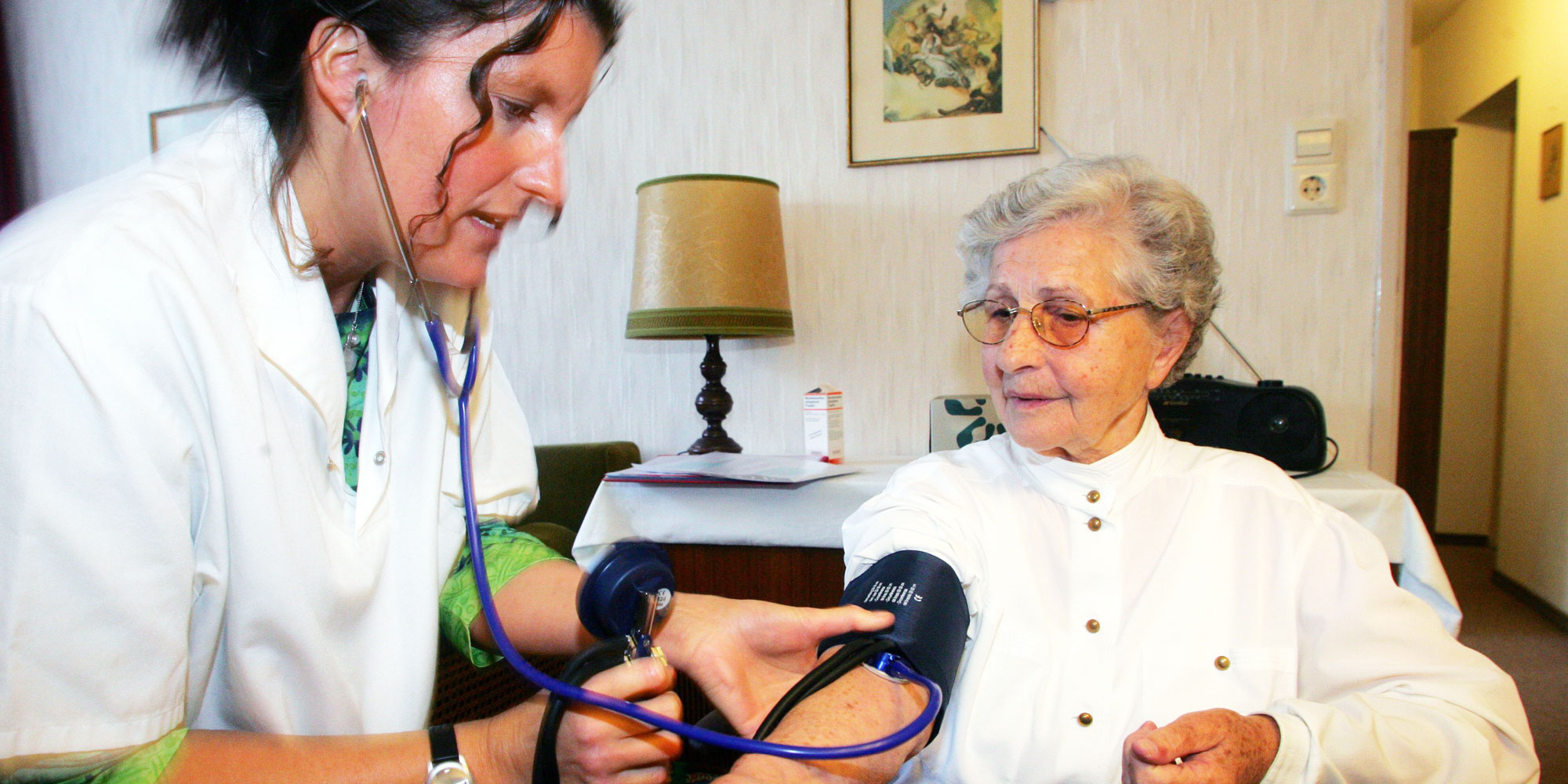 Sjuksköterska hjälper kvinnlig äldre patient i hemmet.