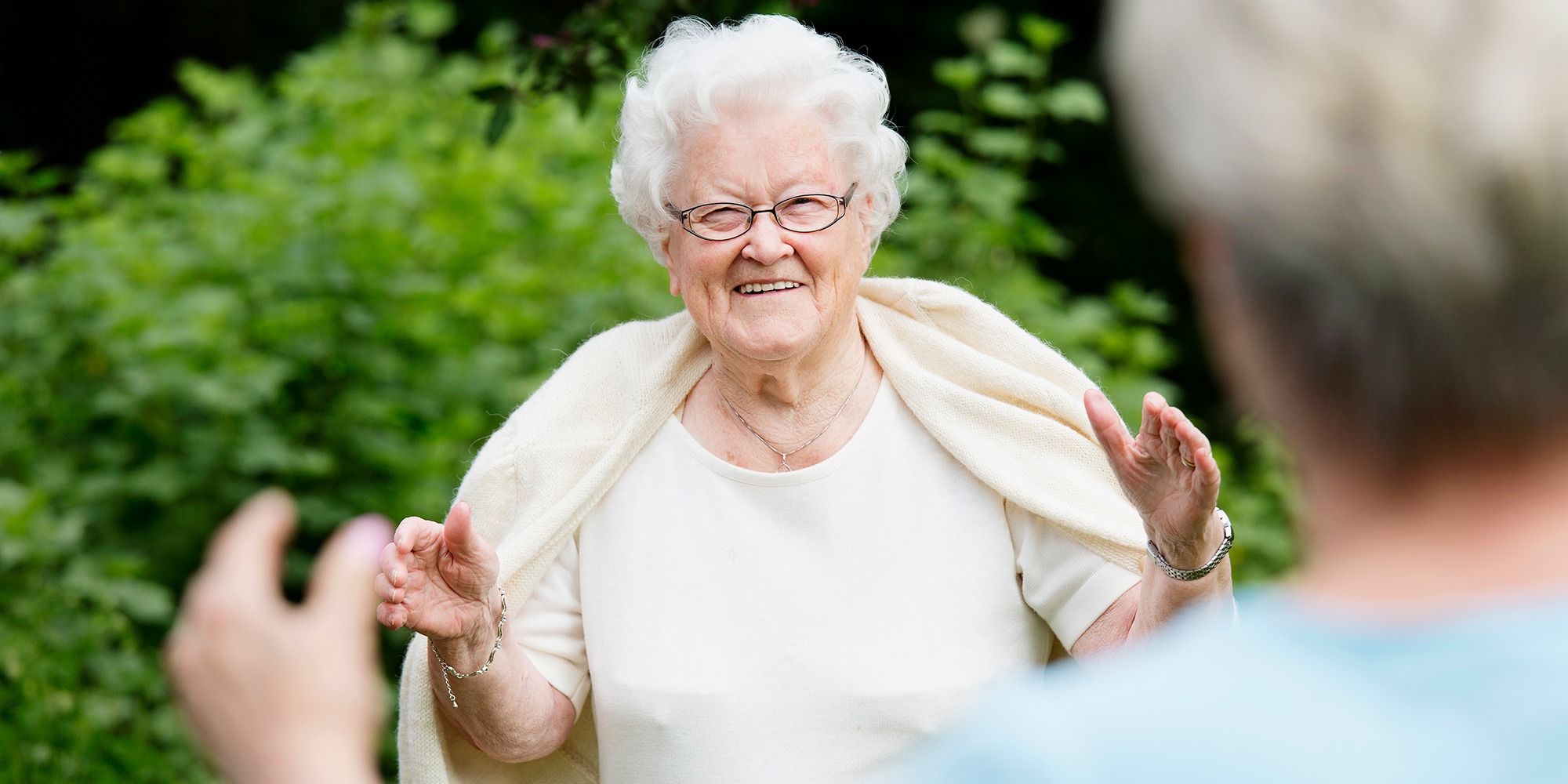 Äldre dam möter person med öppna armar och social distans.