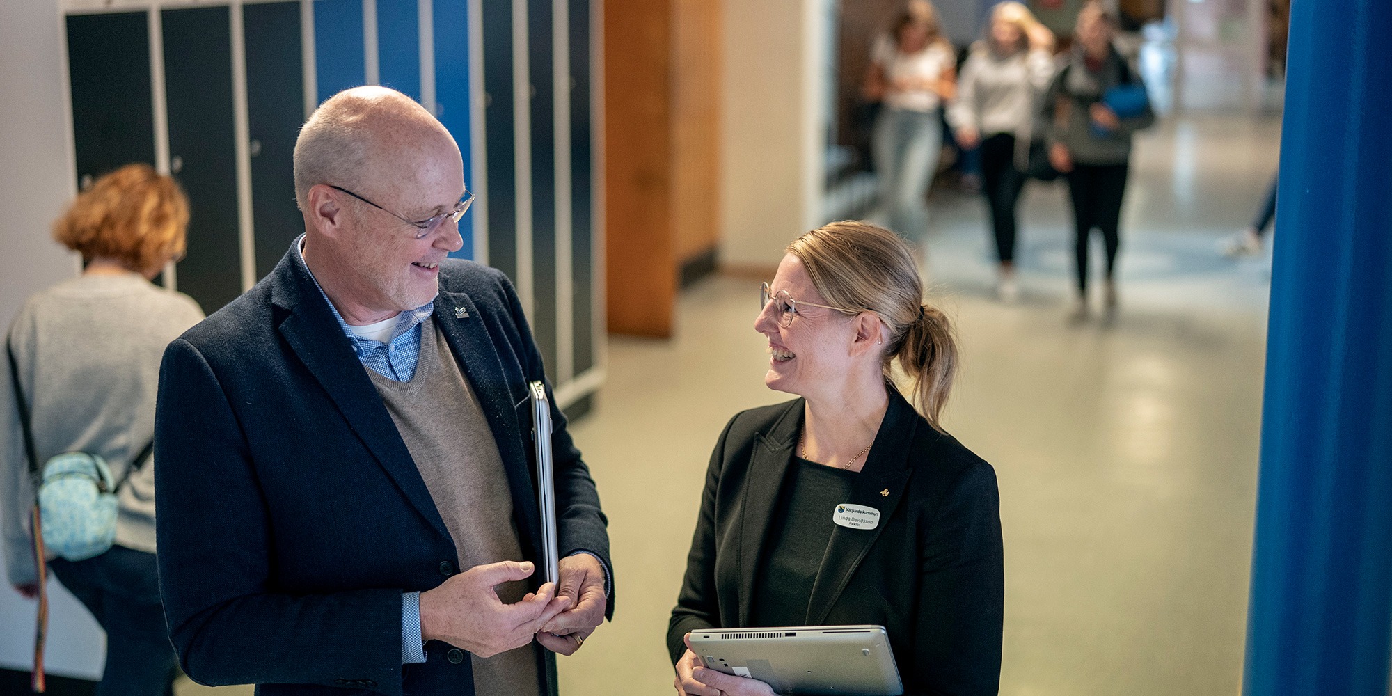 Thomas Stenseke Larsson och Linda Davidsson, rektorer på Gullhögskolan i Vårgårda. De står i en korridor med skåp och elever.