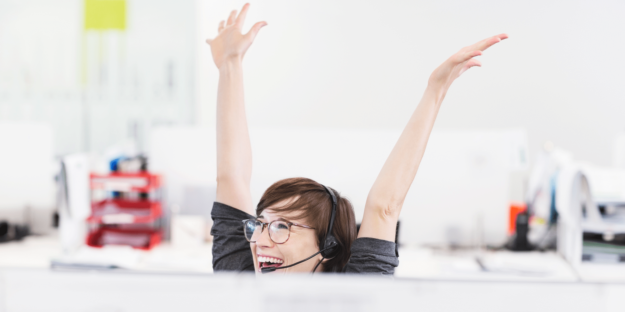 En kvinna sitter vid en dator och ser överlycklig ut samtidigt som hon sträcker upp händerna i luften.