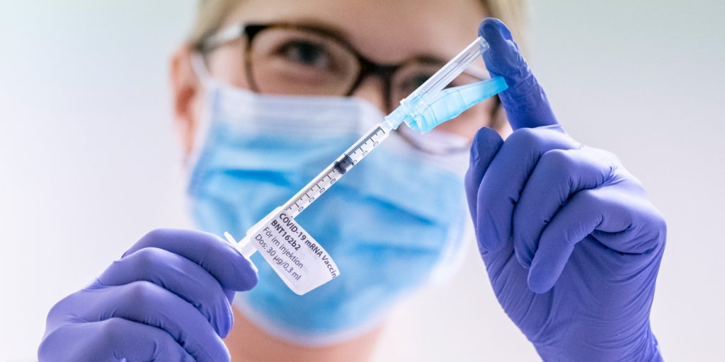Kvinna med skyddsutrustning och vaccinspruta