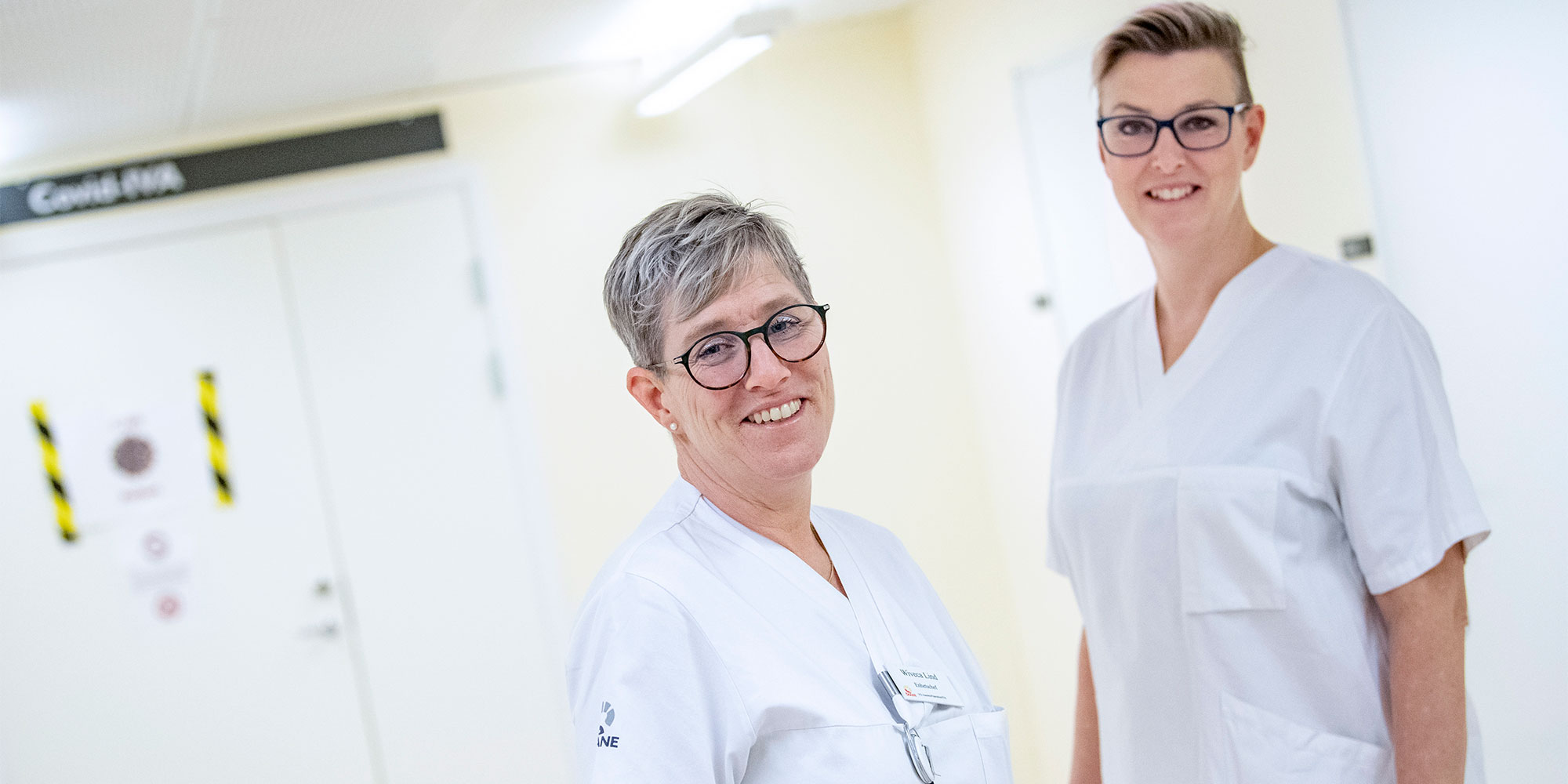 Wiveca Lind och Lisa Hassel står i vita vårdkläder i en sjukhuskorridor.