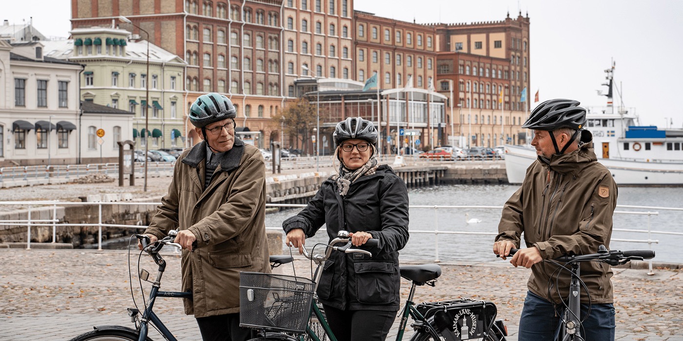 De tar cykeln till jobbet! Tre personer står utomhus med cyklar och cykelhjälmar.