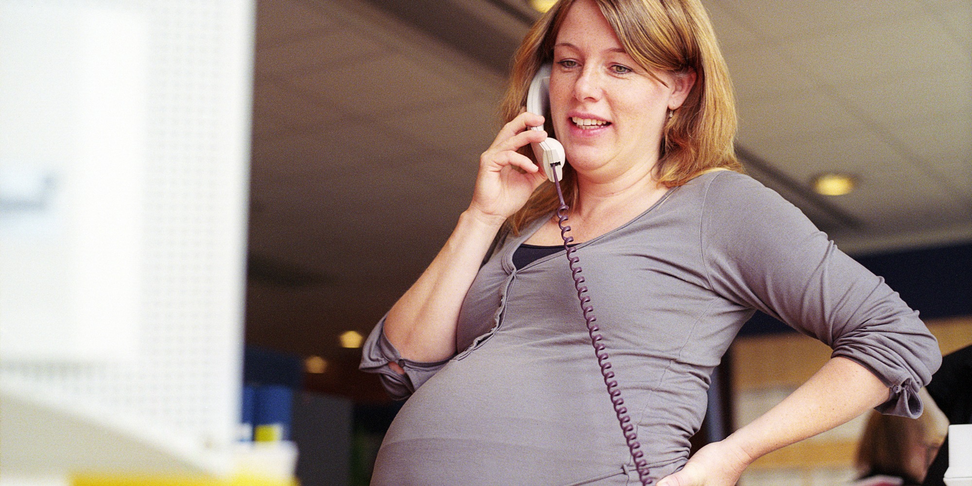 Gravid kvinna talar i telefon i en kontorsmiljö.