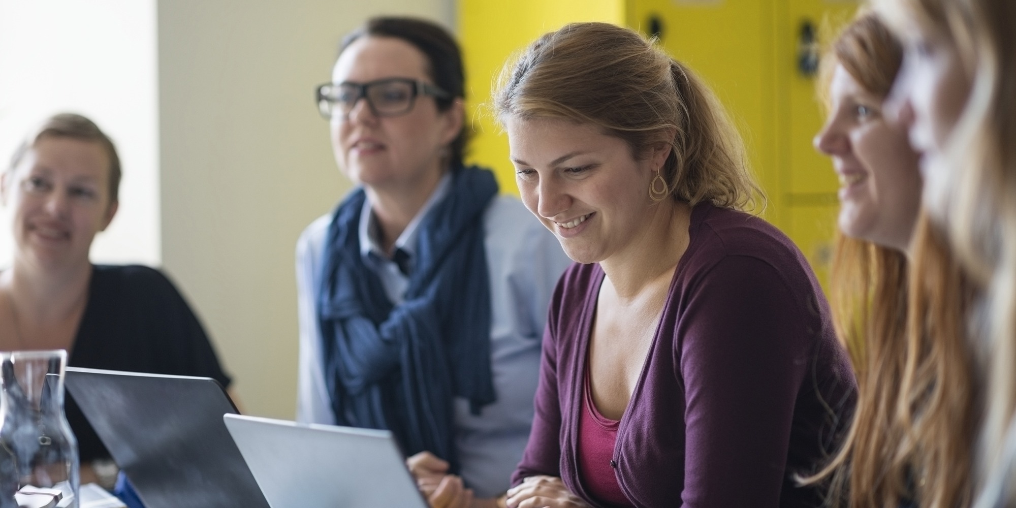 Leende kvinnor vid bord med laptops, bra social arbetsmiljö.