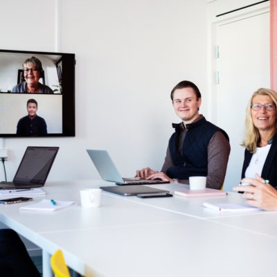 En grupp personer i ett rum har videomöte med en annan grupp personer