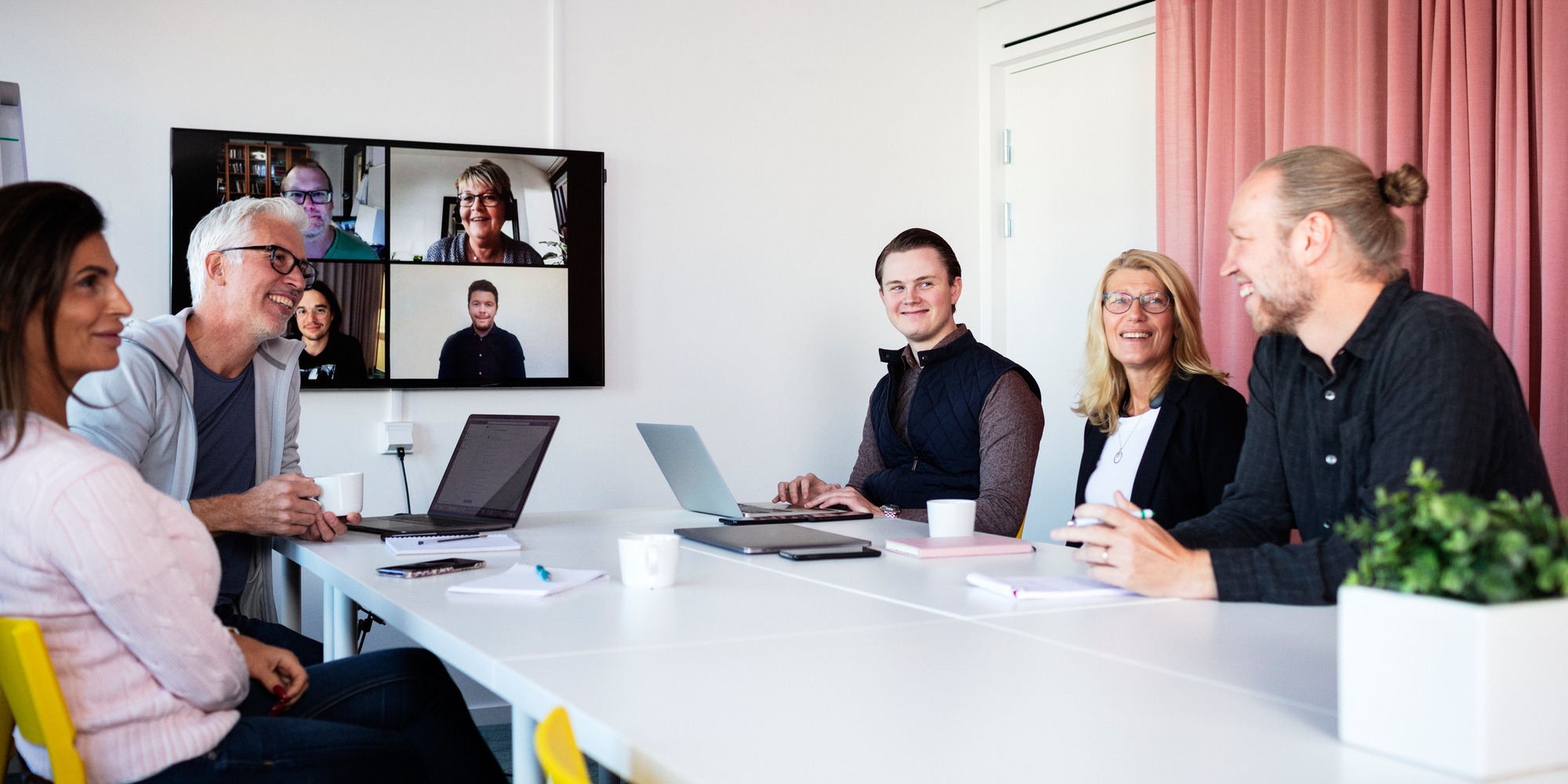 En grupp personer i ett rum har videomöte med en annan grupp personer