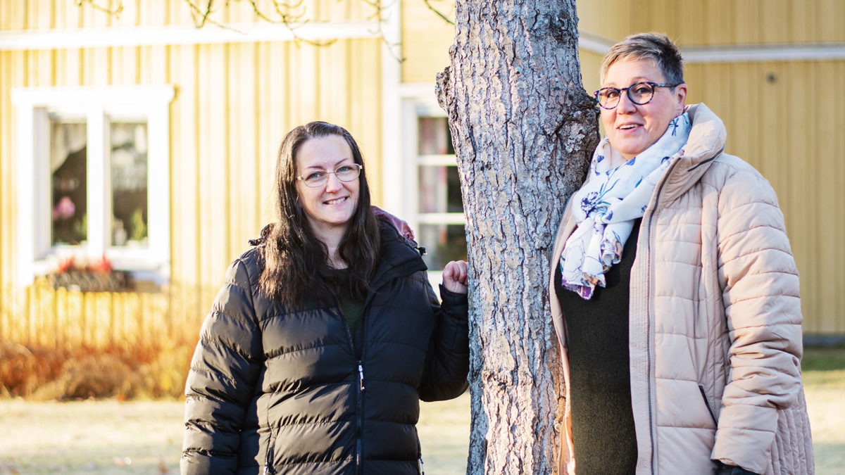 Skyddsombudet Petra Monwell och enhetschefen Madelen Karlsson vid et träd i vintersol utanför en gul vacker träbyggnad, Brismarksgården i Hoting, Strömsunds kommun.