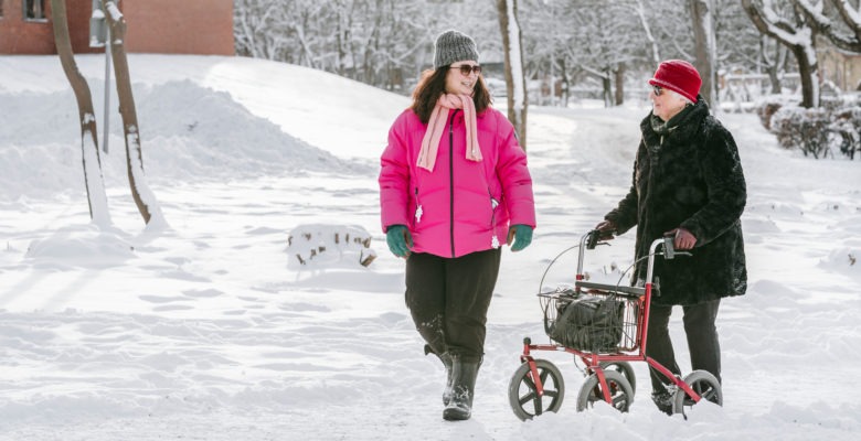 Äldre kvinna och yngre går med rullator i snö