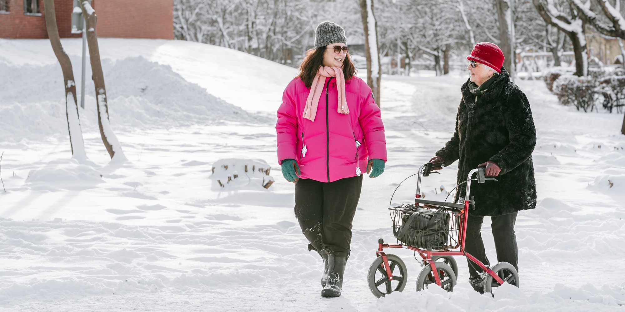 Äldre kvinna och yngre går med rullator i snö.