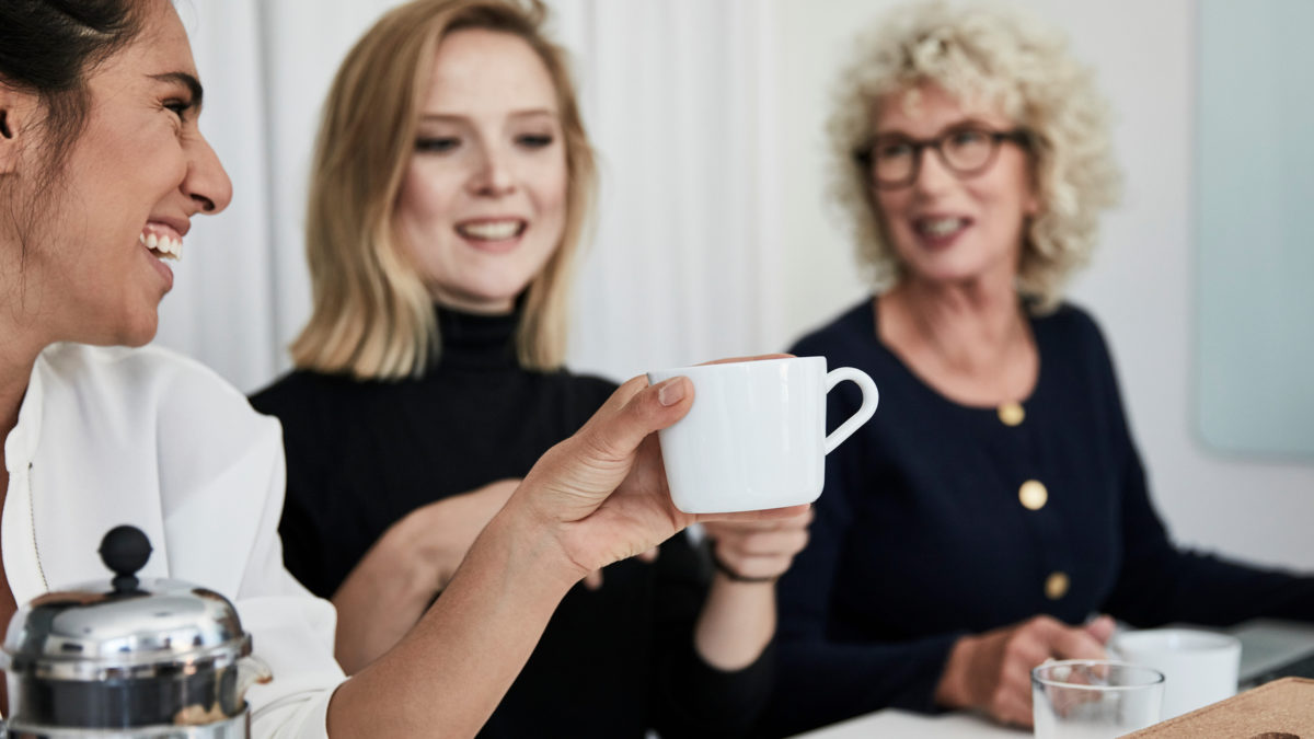 Tre kvinnor i ett mötesrum häller upp kaffe